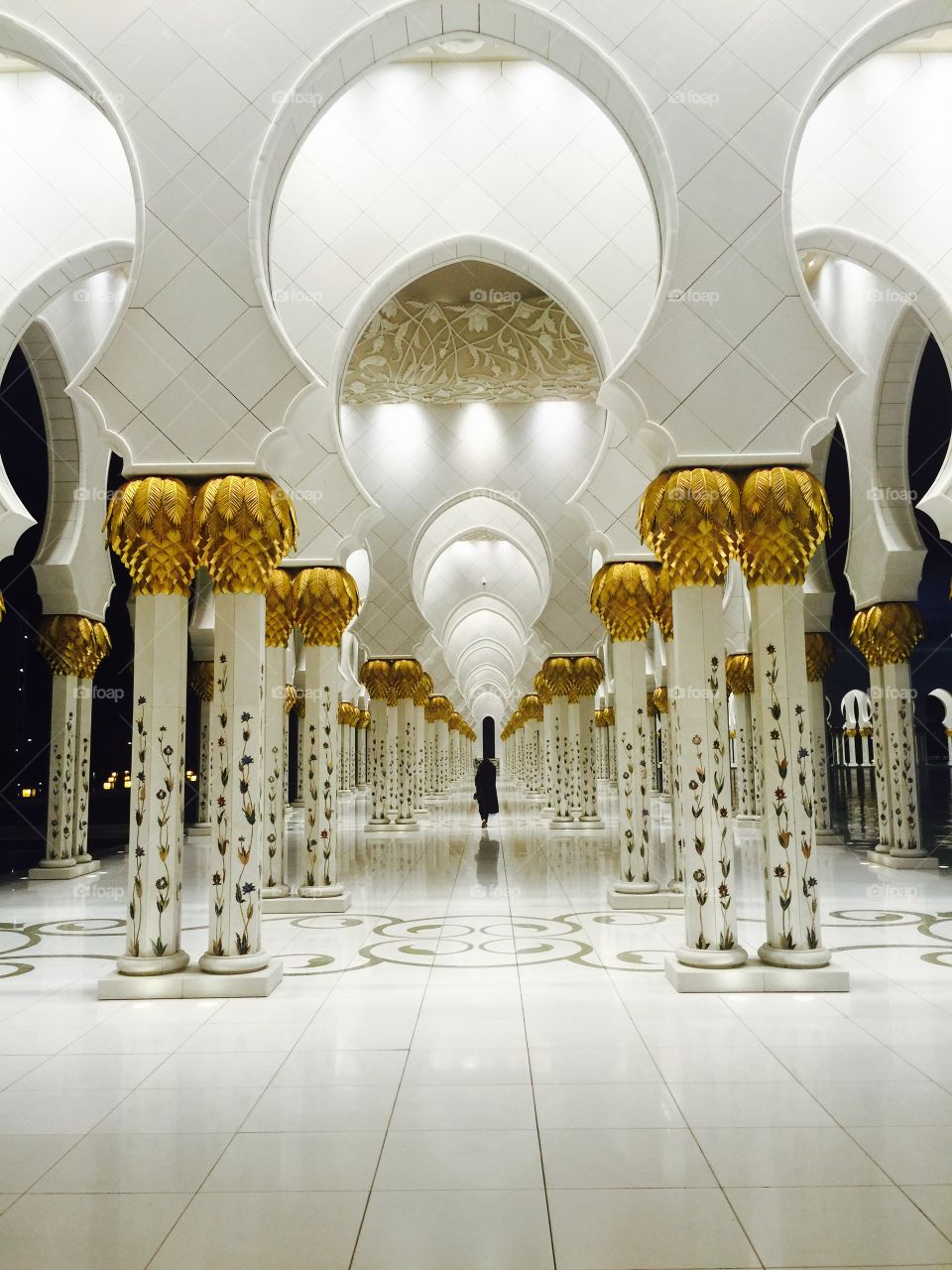 Woman walking between Gold mosaic pillars and arches at the Sheikh Zayed Grand Mosque 