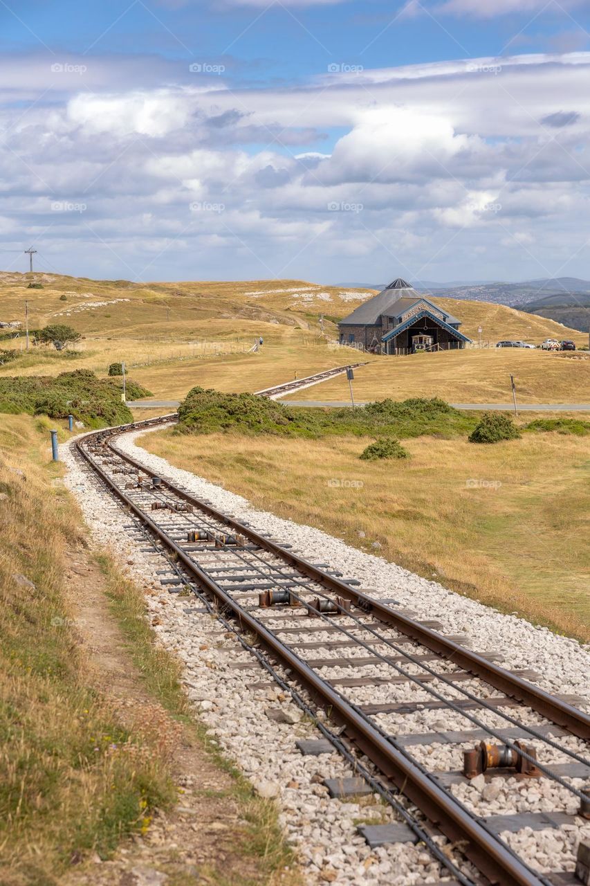 Single train track leading to a station through yellow and green grassy countryside