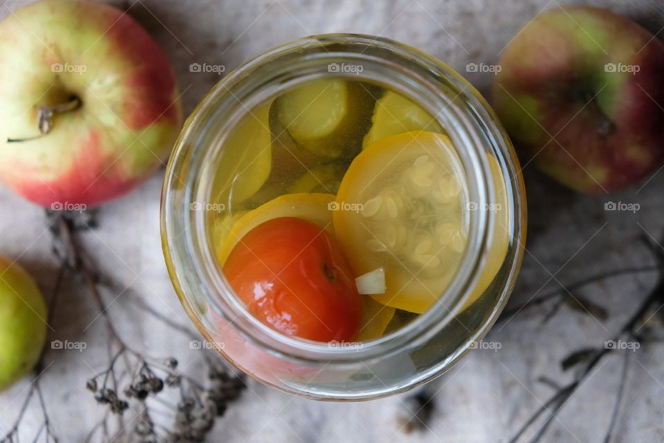 Opened glass jar with pickled vegetables and apples on the background