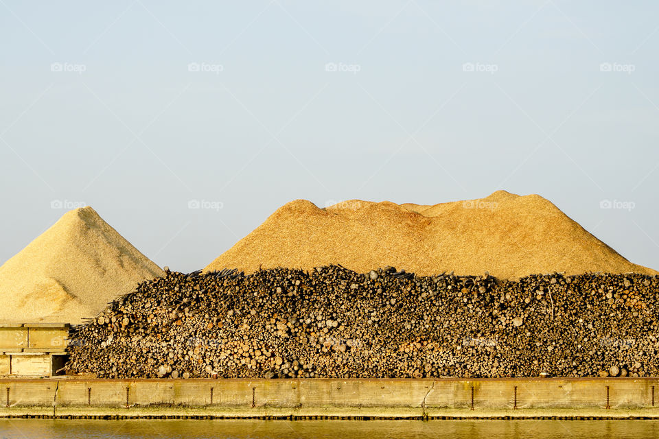big piles of wooden logs and wood chips under blue sky in the harbor
