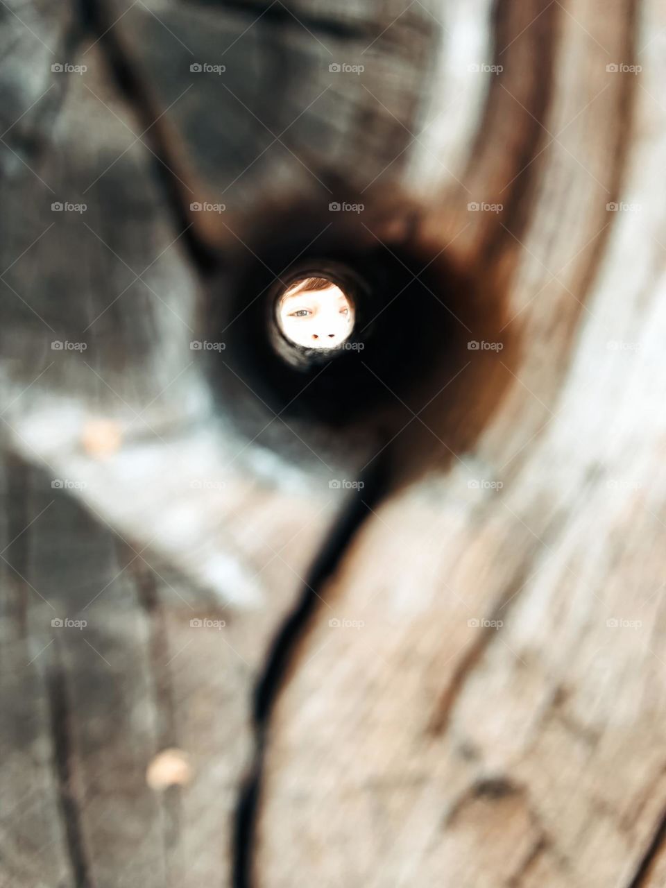 Close up of a wooden hole with a face at the other side