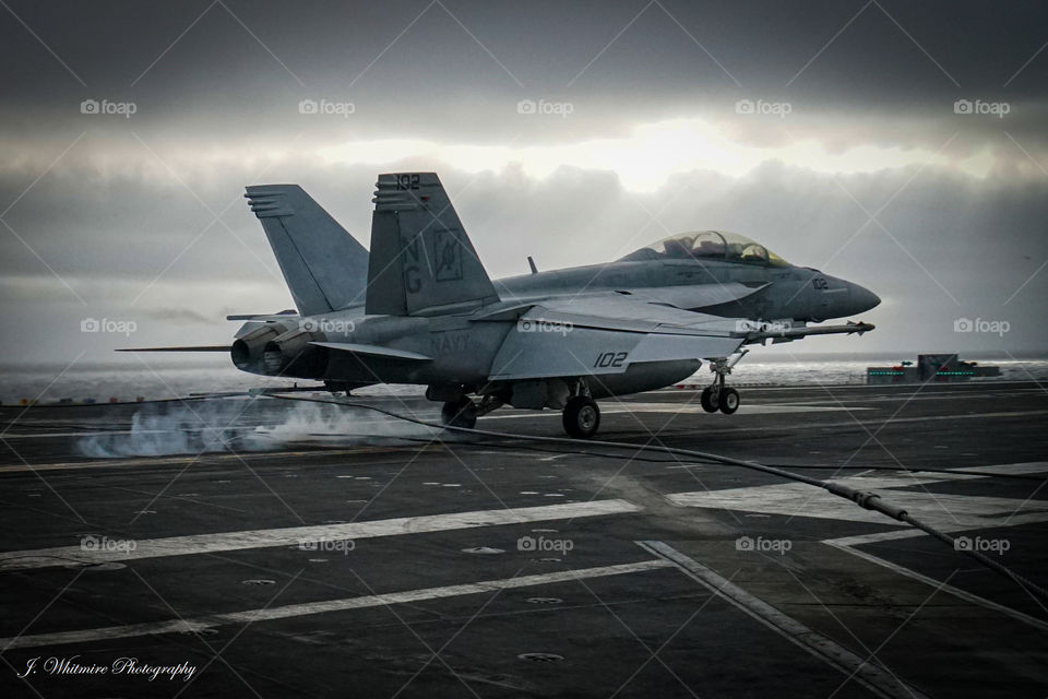A F/A-18 Super Hornet catches the third wire on a aircraft carrier deck