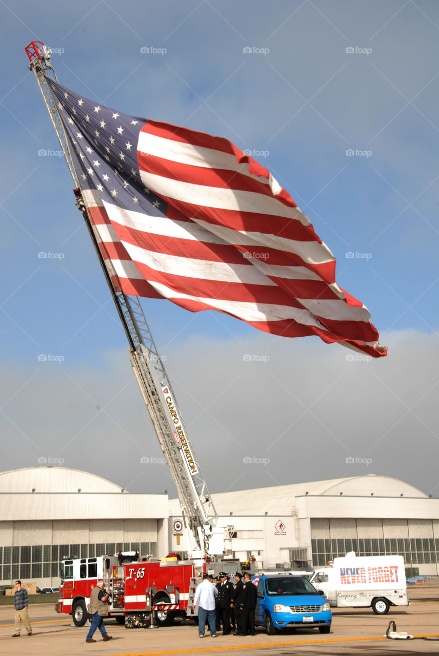 A extremely large American flag at the top of a ladder of a fire engine!