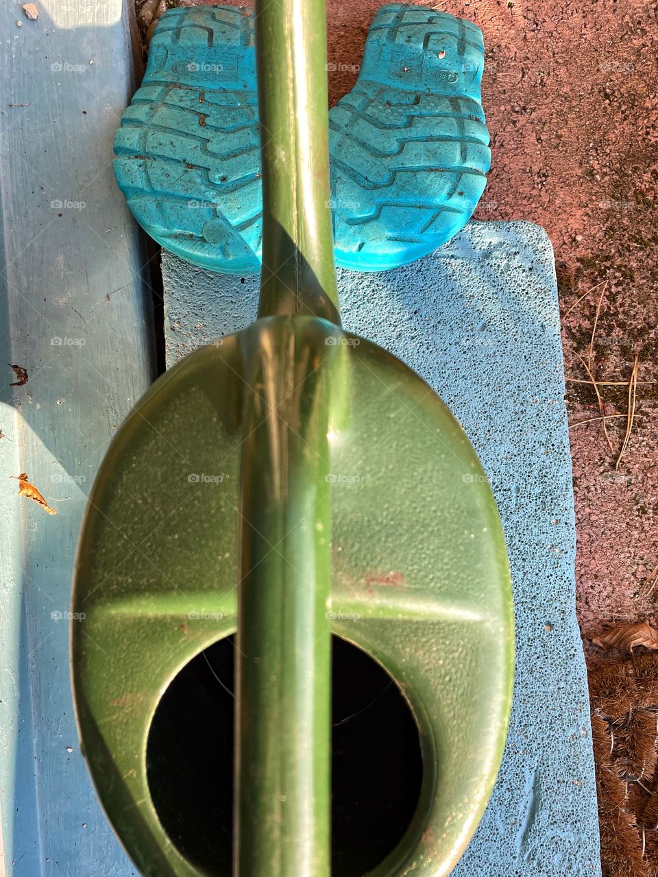 Close-up of a green watering can and blue garden shoes from above