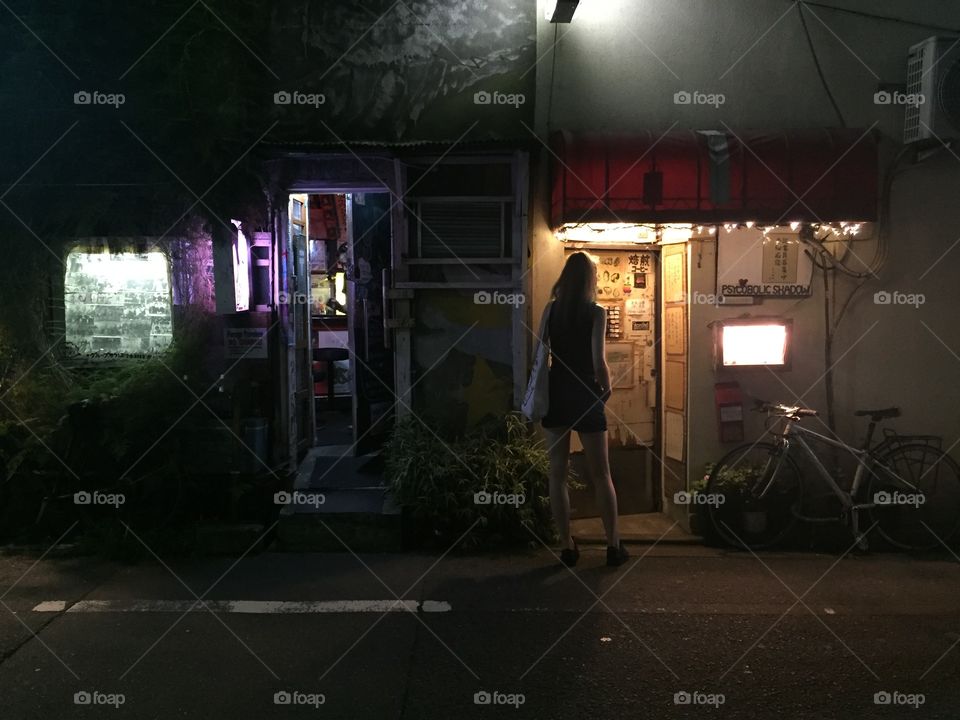 Colorful city lights in golden gai backalley in tokyo. A girl is looking at the bars