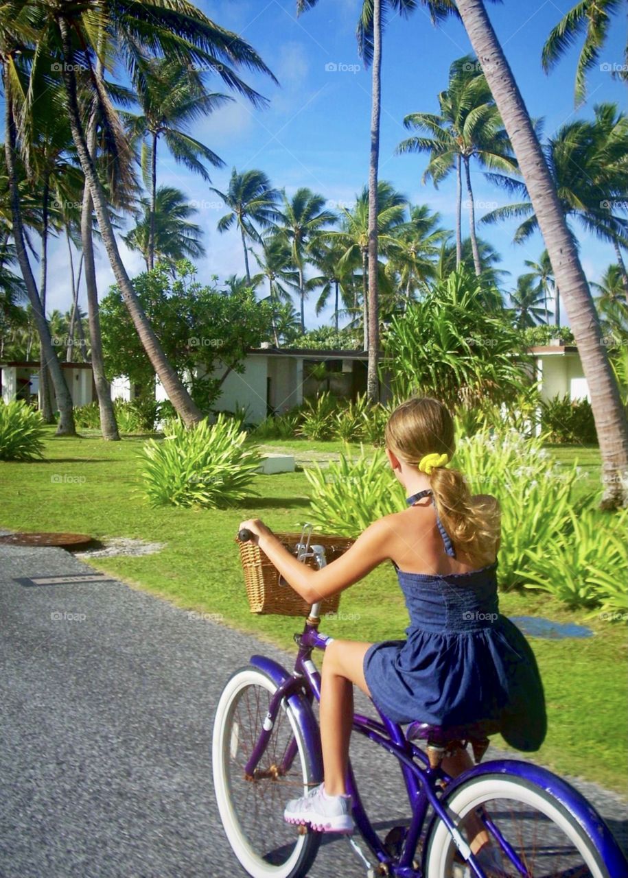 A young girl rides her bike along a palm tree lined street on Kwajalein Atoll, Marshall Islands 