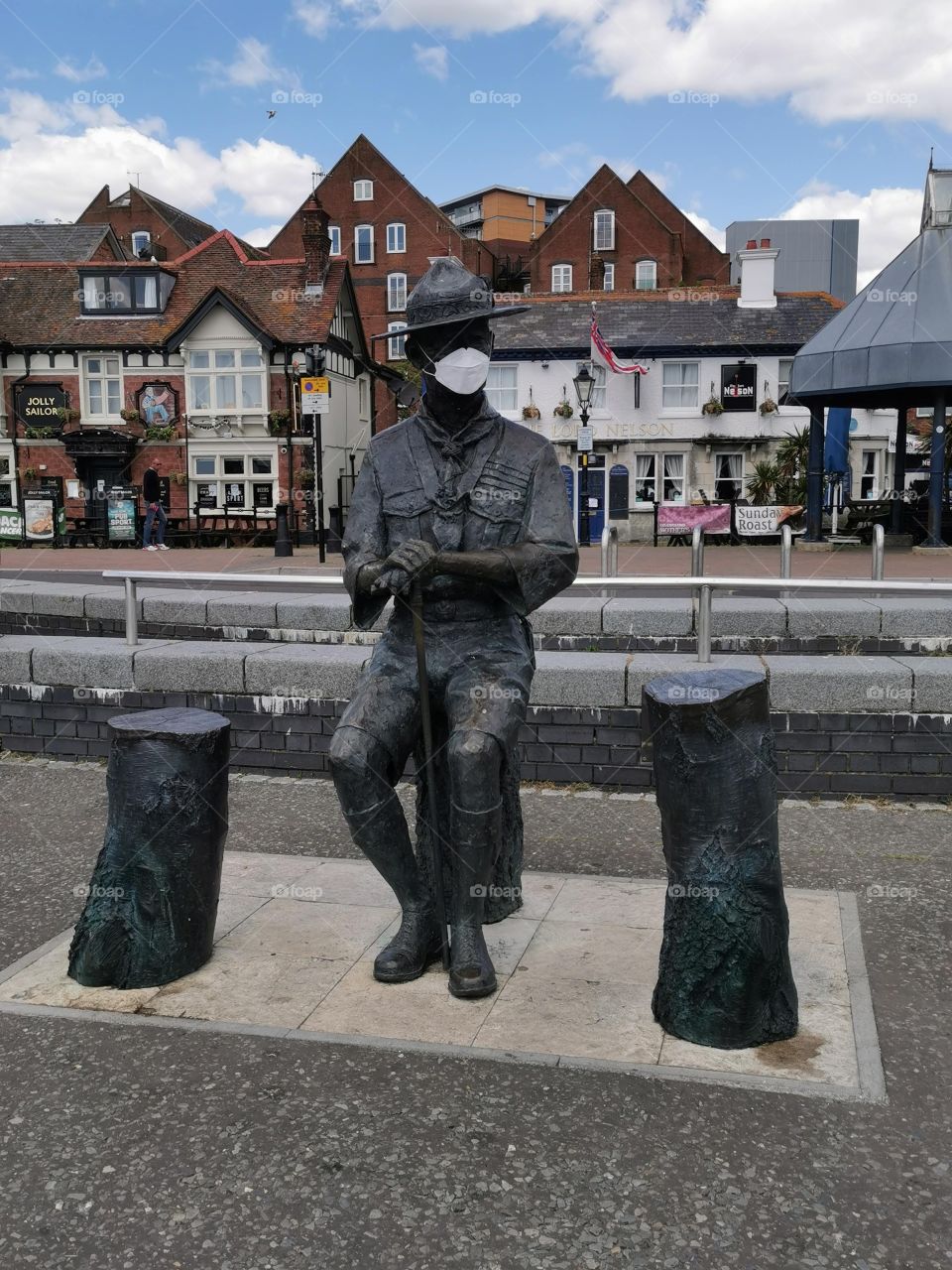 Statue of Robert Baden-Powell with Covid-19 protection at Poole Quay in Dorset with the Jolly Sailor Pub and the Lord Nelson Pub in the background