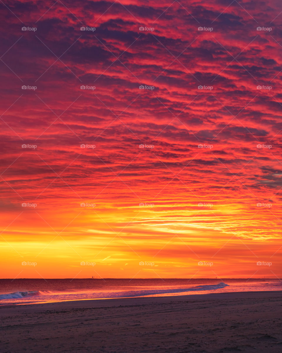 Beautiful intense vibrant colors lighting up rippled altocumulus clouds during sunset, above a peaceful beach. 