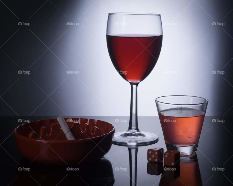 dark poker style image with red dice, red wine, red liquor shot, and red ashtray with cigarette