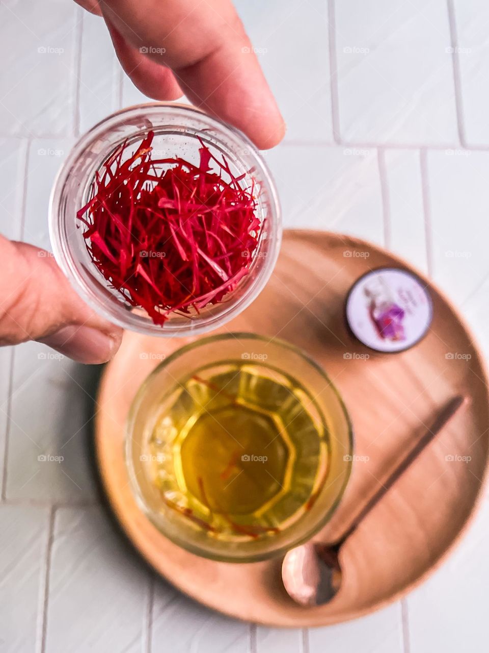 Saffron in a round clear case and a cup of hot water with saffron in it 