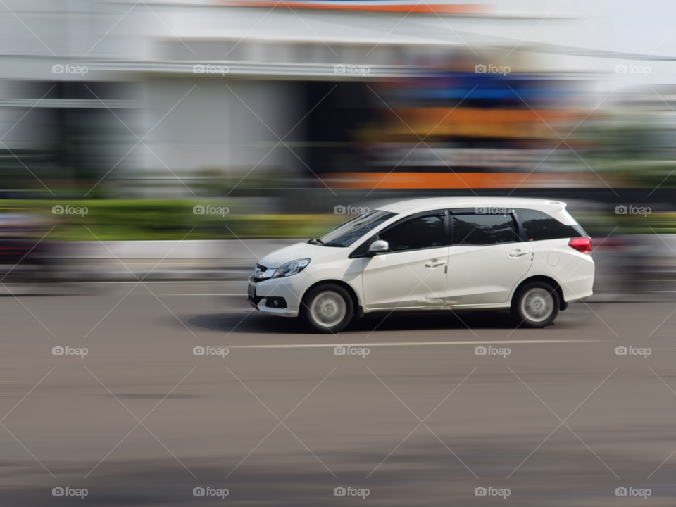 Driving car on highway, multi purpose vehicle type car, MPV, multipurpose transportation vehicle, passenger car, much liked by general public, on the main streets of the city Bandung, Indonesia, clean white color,