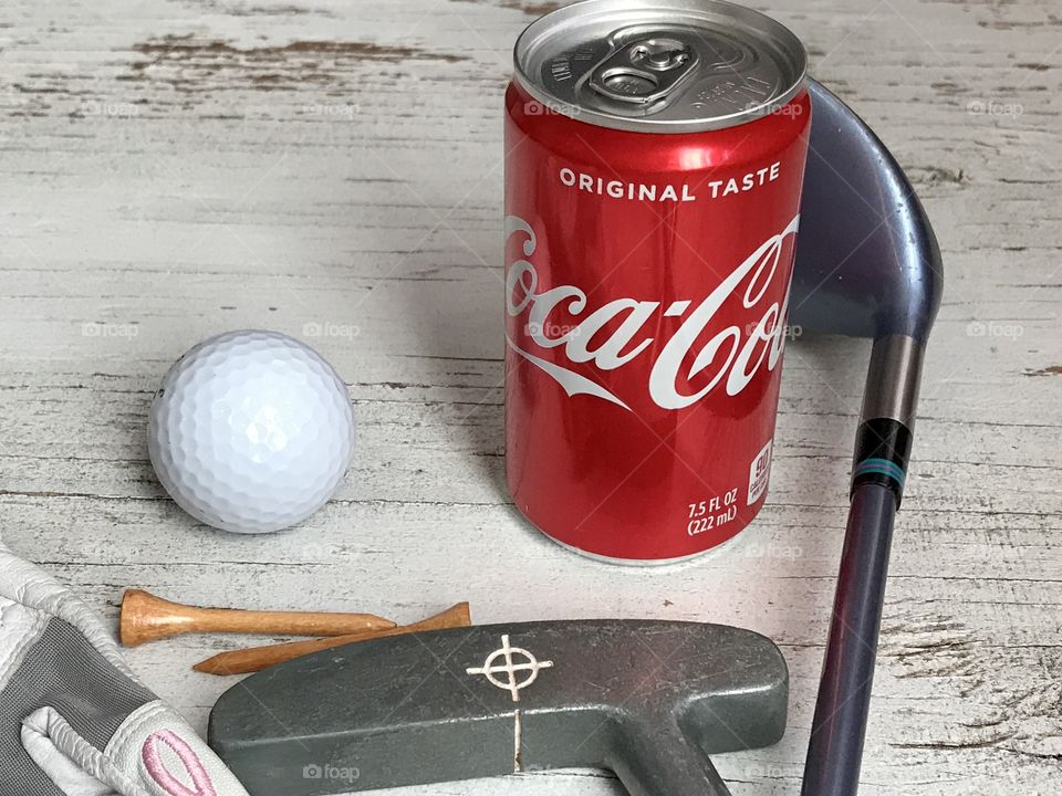 A can of Coca Cola with golf equipment on a white rustic background 