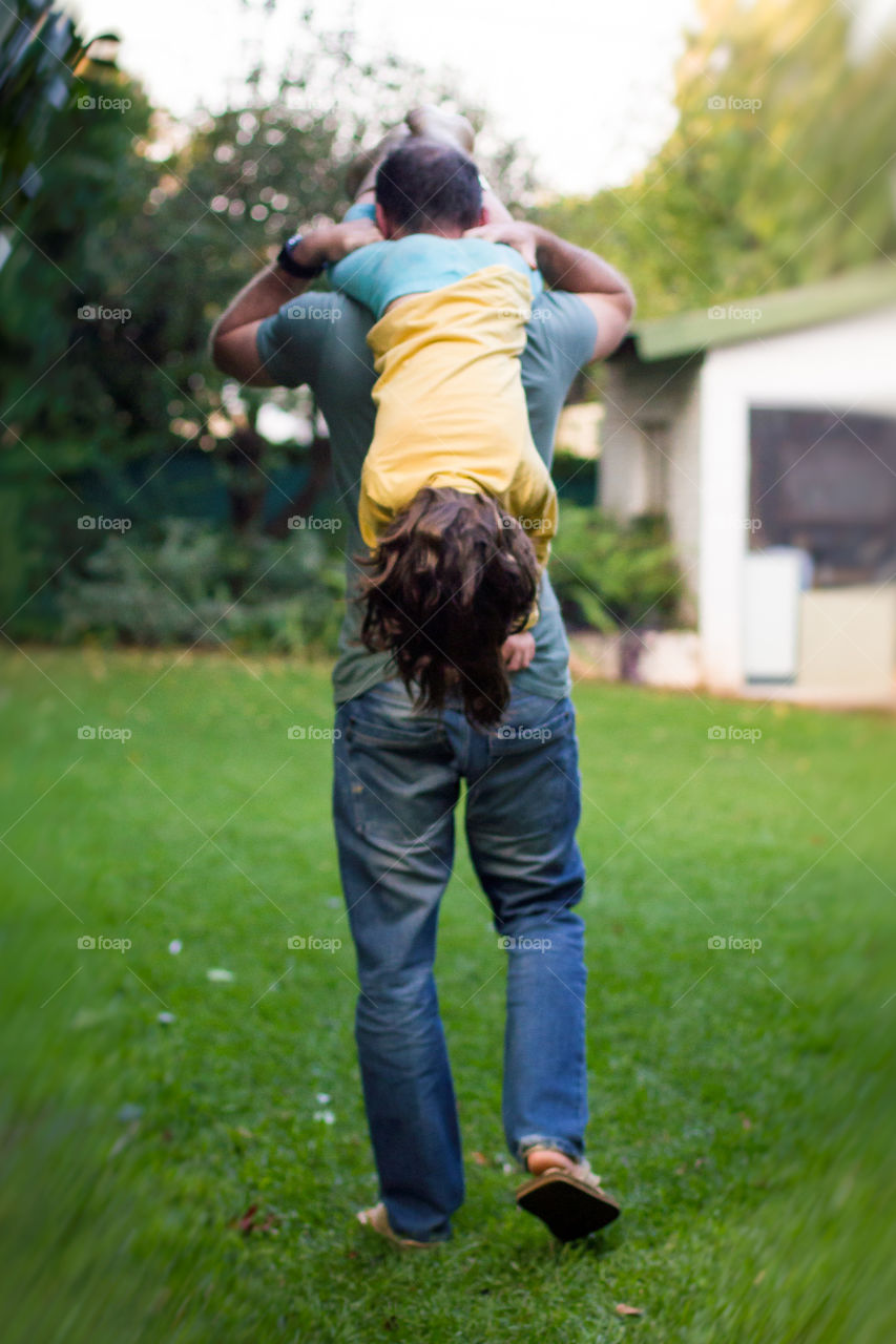 Staying fit during covid19 at home - image of man doing exercise in the garden with girl over his shoulder - fitness is fun and family time at the same time!