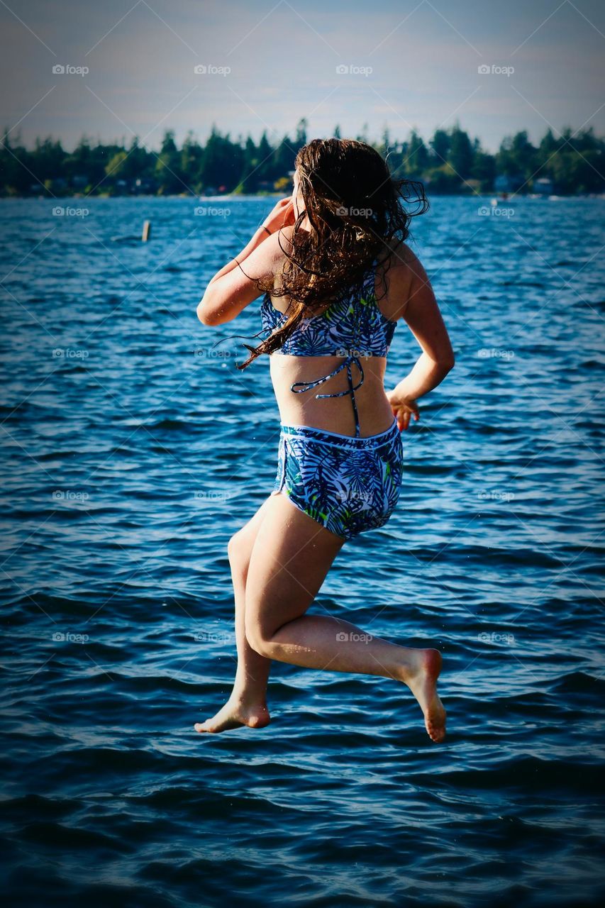 A young woman wearing a blue print bathing suit jumps into a bright blue lake while enjoying the warm summer days in Washington State