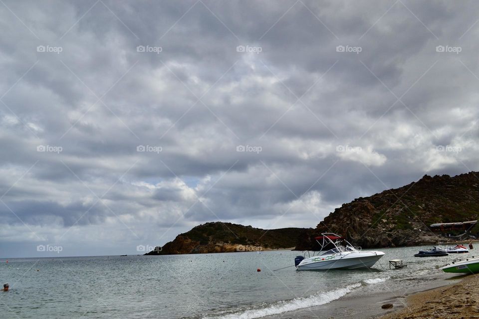 Beautiful landscape of storm clouds over the sea, a small yacht and mountains in the background