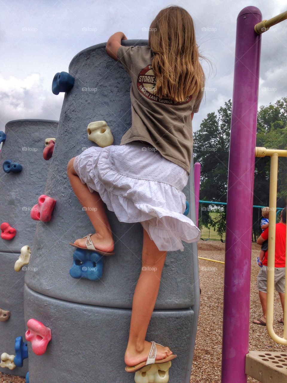 Almost there. Girl climbing the Rock wall at the park