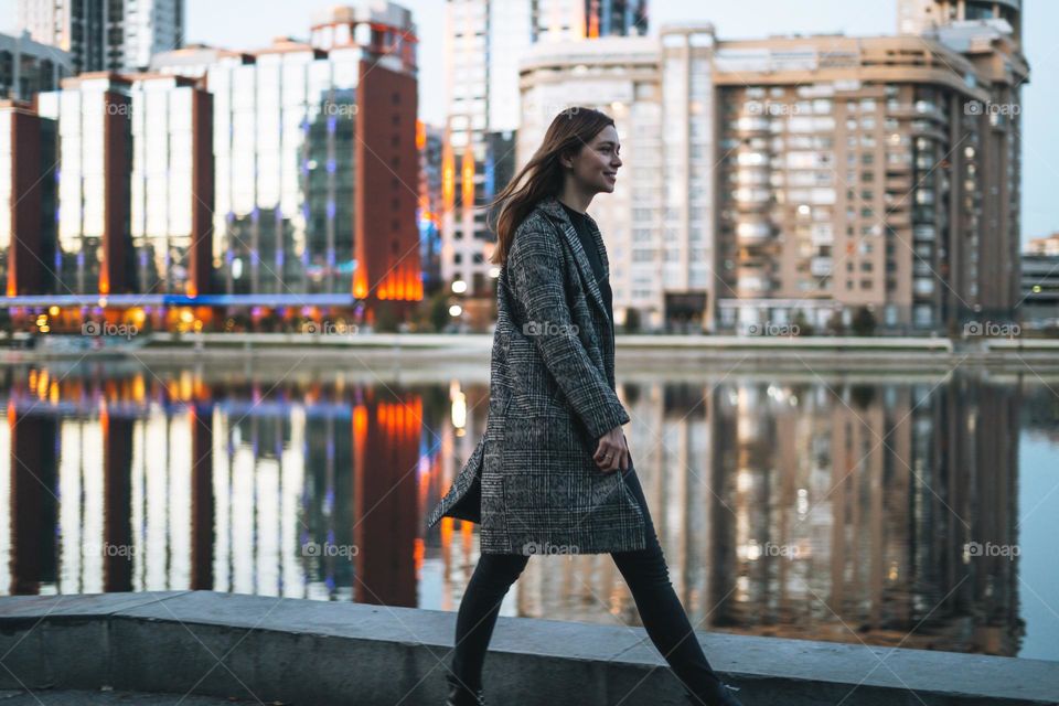 Young woman walking on street near city river at night 