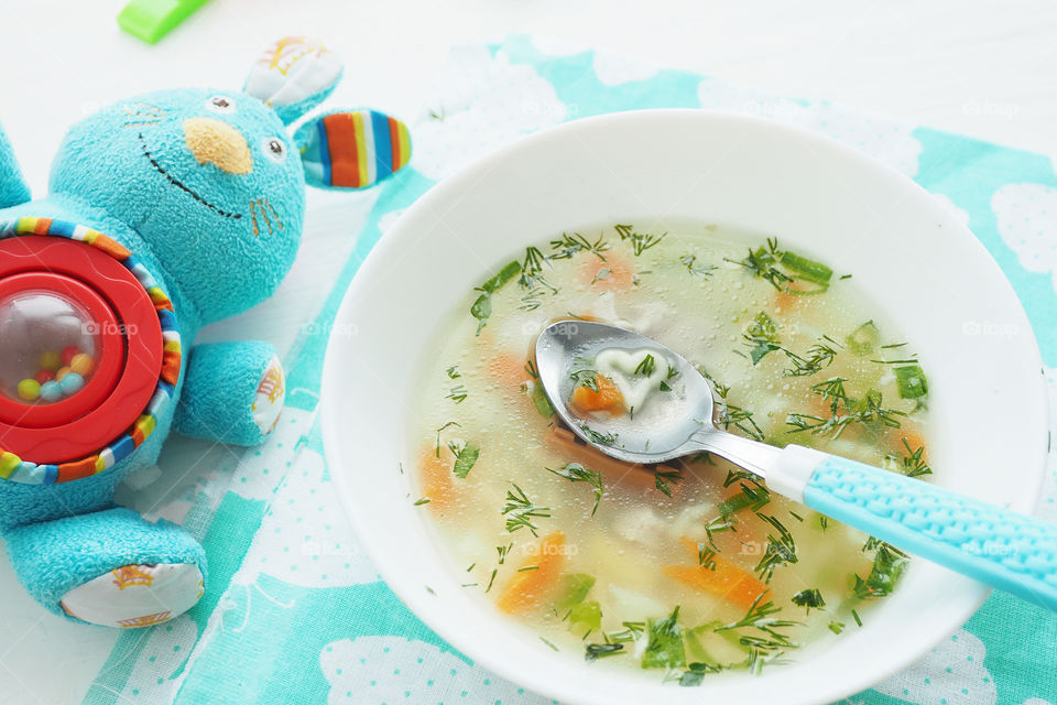 a plate of soup with noodles and herbs, a spoon and a rabbit toy