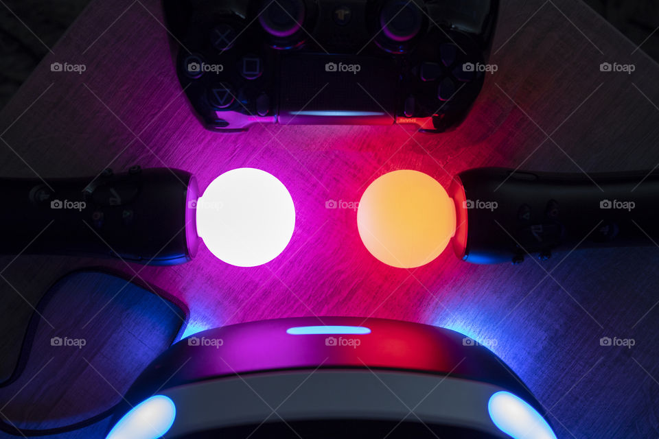 A light scenic portrait of a turned on PlayStation vr controllers, ps4 controller and vr headset. with the lights of the technologies casting great colors.