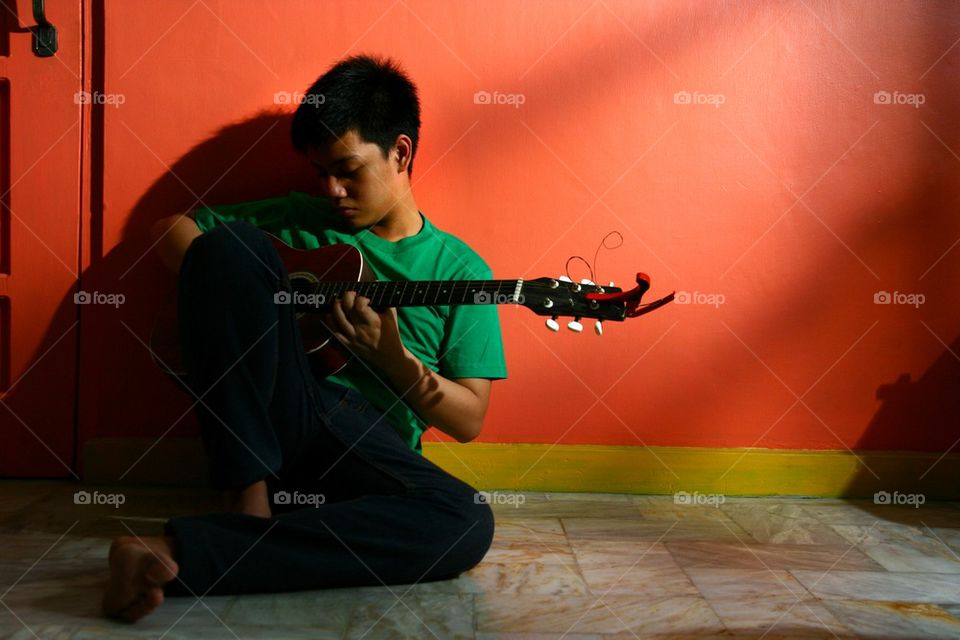 young asian teen playing guitar in a living room