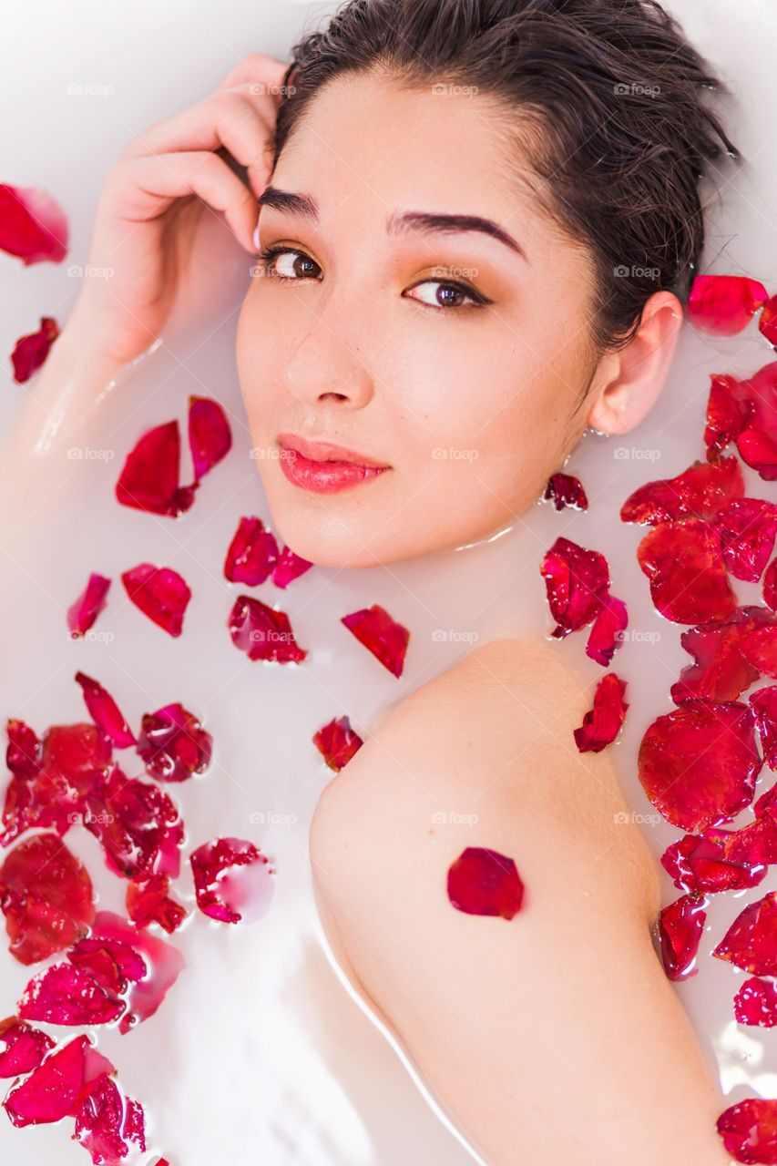 Beautiful girl in milk bath with red rose petals. Portrait, close-up