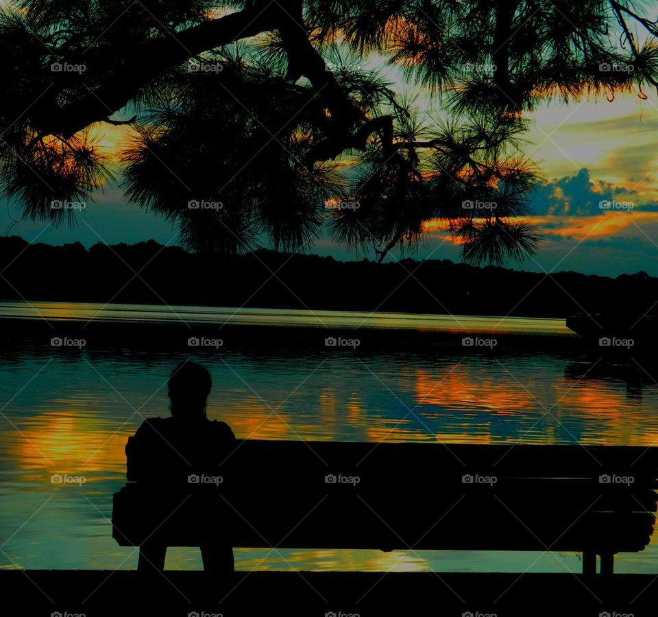 Silhouette of a person sitting on bench and looking at view during sunset
