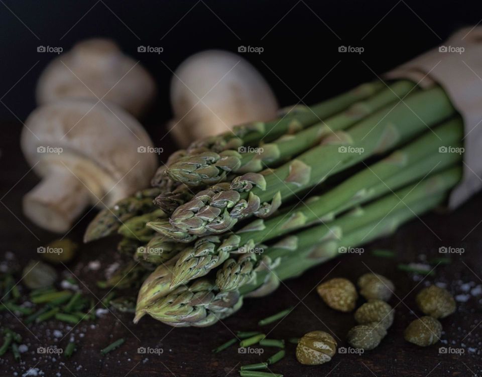 Asparagus spears, mushrooms, capers & chopped chives on a dark wood board