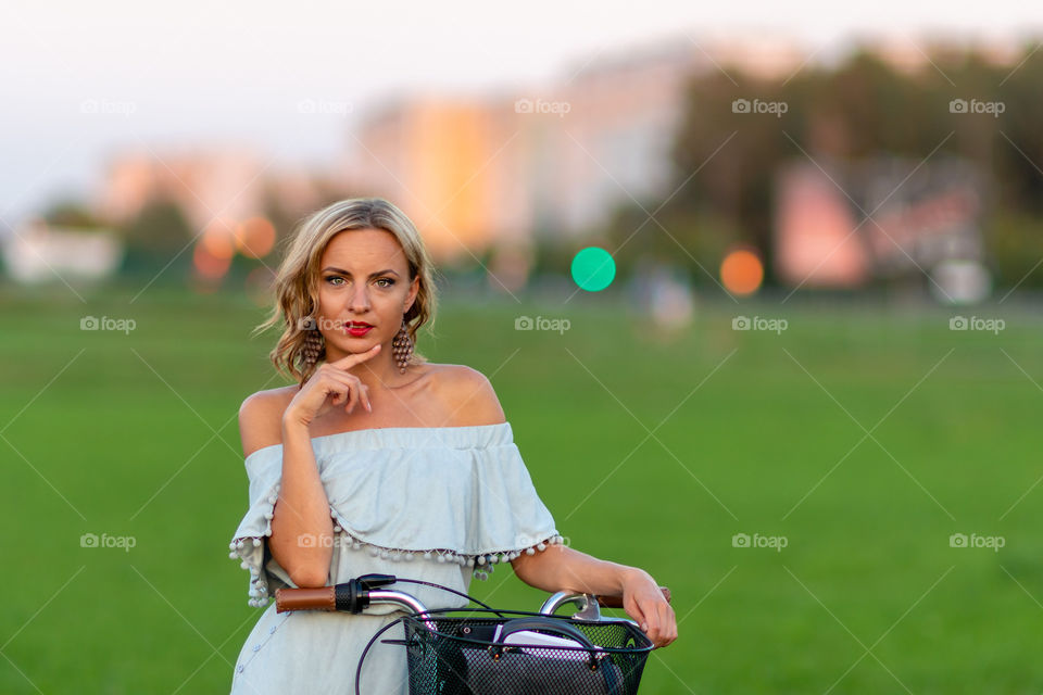 Soft focus photo. A young, beautiful blond woman with a white bike in a green meadow.
