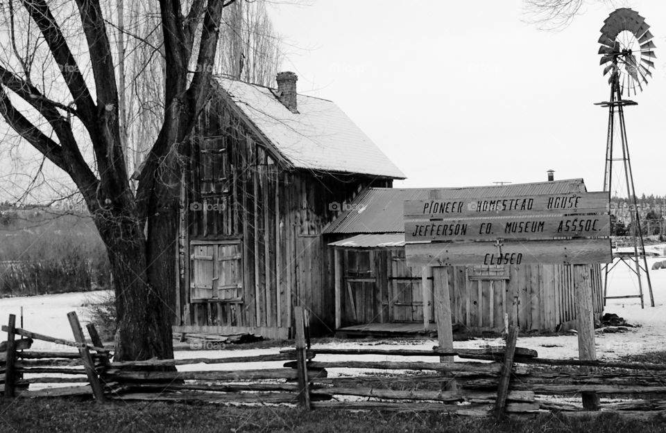 The Pioneer Homestead House in Madras in Central Oregon surrounded by a wooden fence with snow on the ground on a cold winter day. 