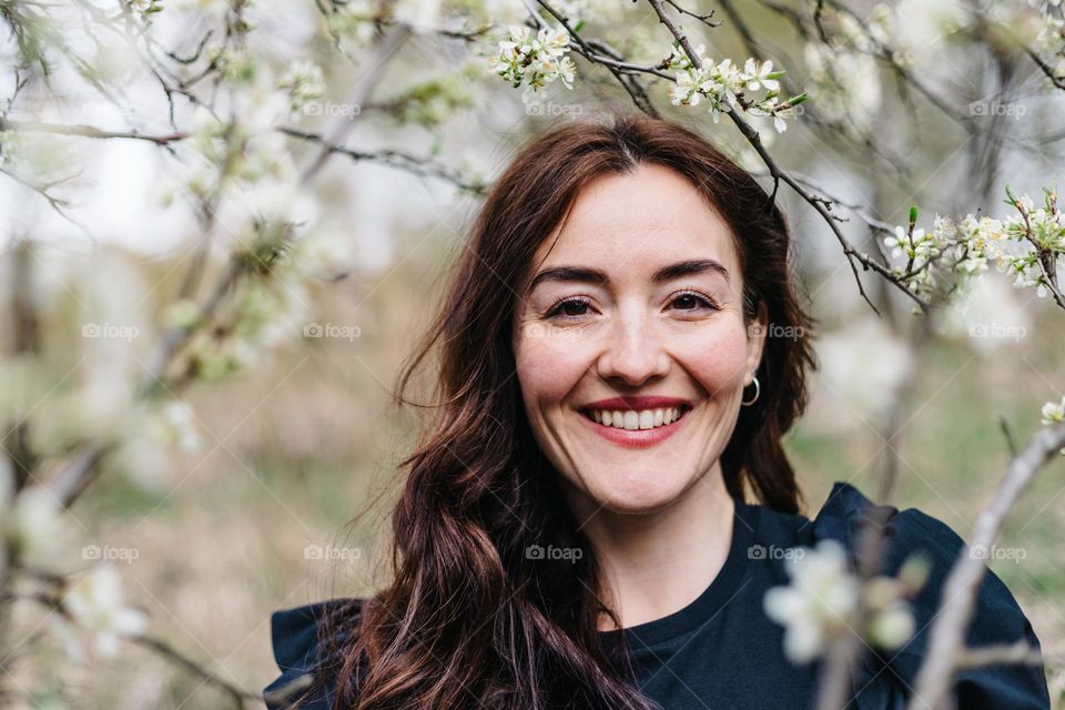 Portrait of a young beautiful woman, surrounded by blossoming trees, while on a walk on a beautiful spring day.