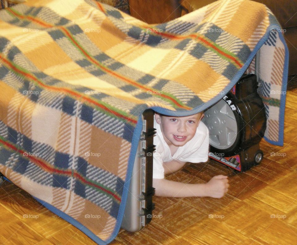 Portrait of happy boy lying under blanket