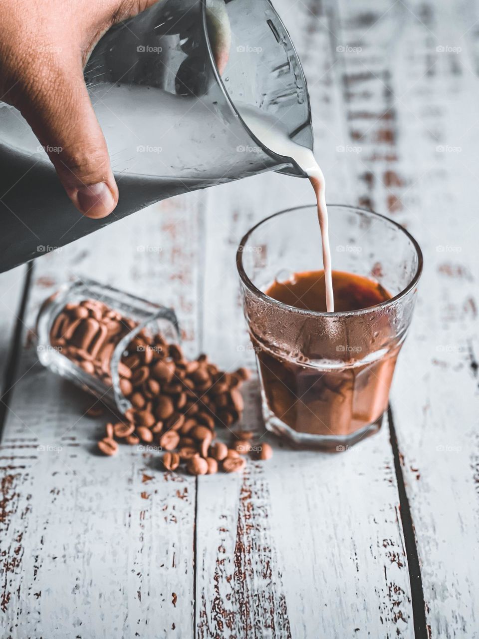 Pouring milk into a cup on black coffee on a wooden table
