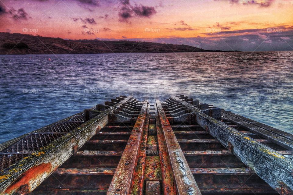 Rusty Slipway. A rusty old lifeboat slipway disappears into a cold Ocean at sunrise.