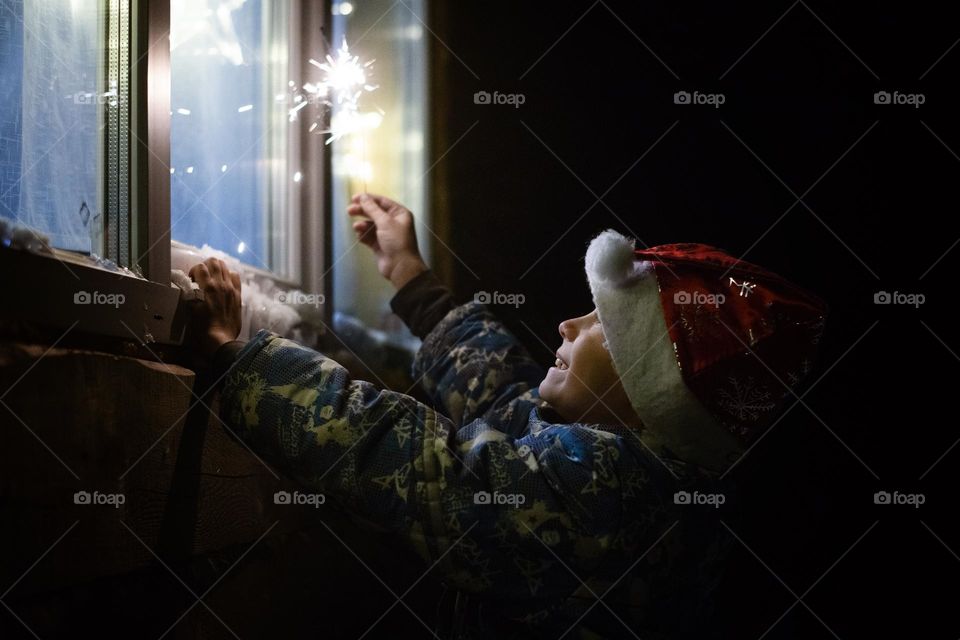 a child in a New Year's hat with sparkler looks out the window