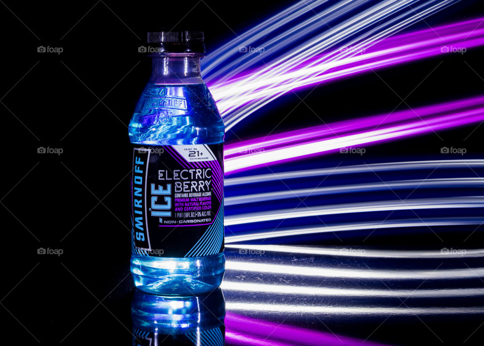 dark image of popular blue drink in a bottle with bright purple, blue, and white light streaks coming out of the bottle