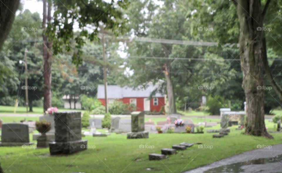 Several gravestones in a cemetery with a small red farmhouse in the background