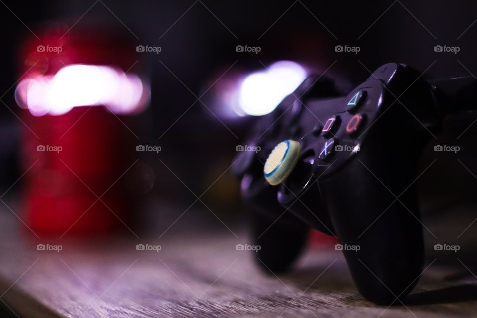 low light photo of single player mode playstation controller gamepad accessories sideway on a wood desk blur background gamer room big boys toys.