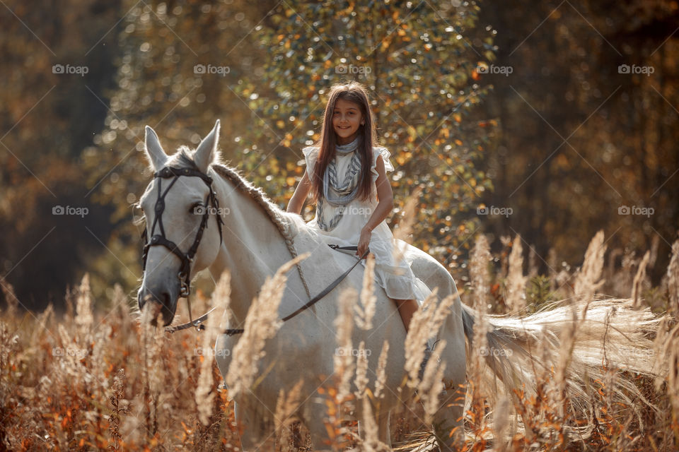 Little girl with grey horse in autumn park 