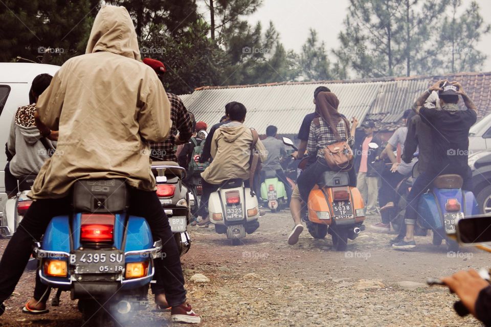 Portrait of a group of Vespa riders photographed from behind during a convoy on a street in bogor driving various types of classic Vespas.