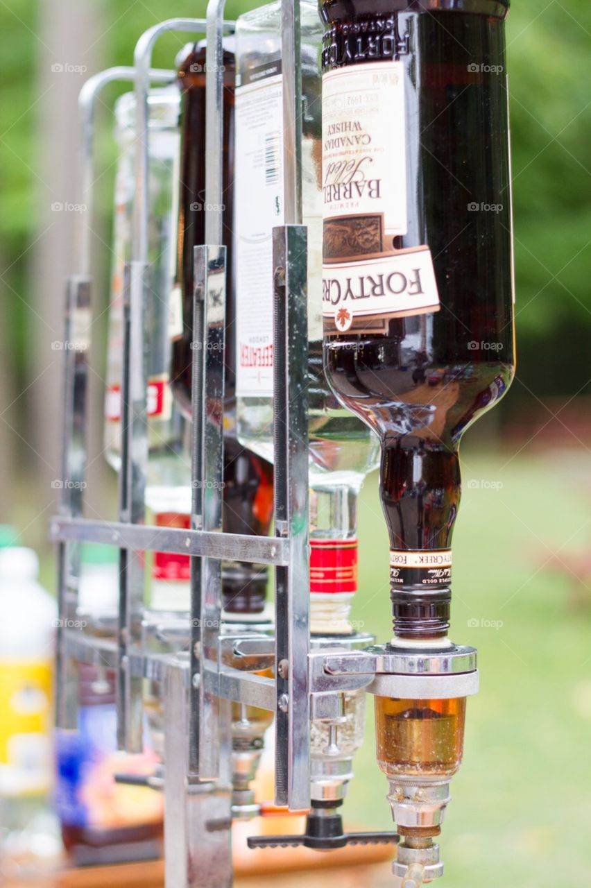 Alcohol bottles stand in a liquor dispenser upside down at a bar that is outdoors