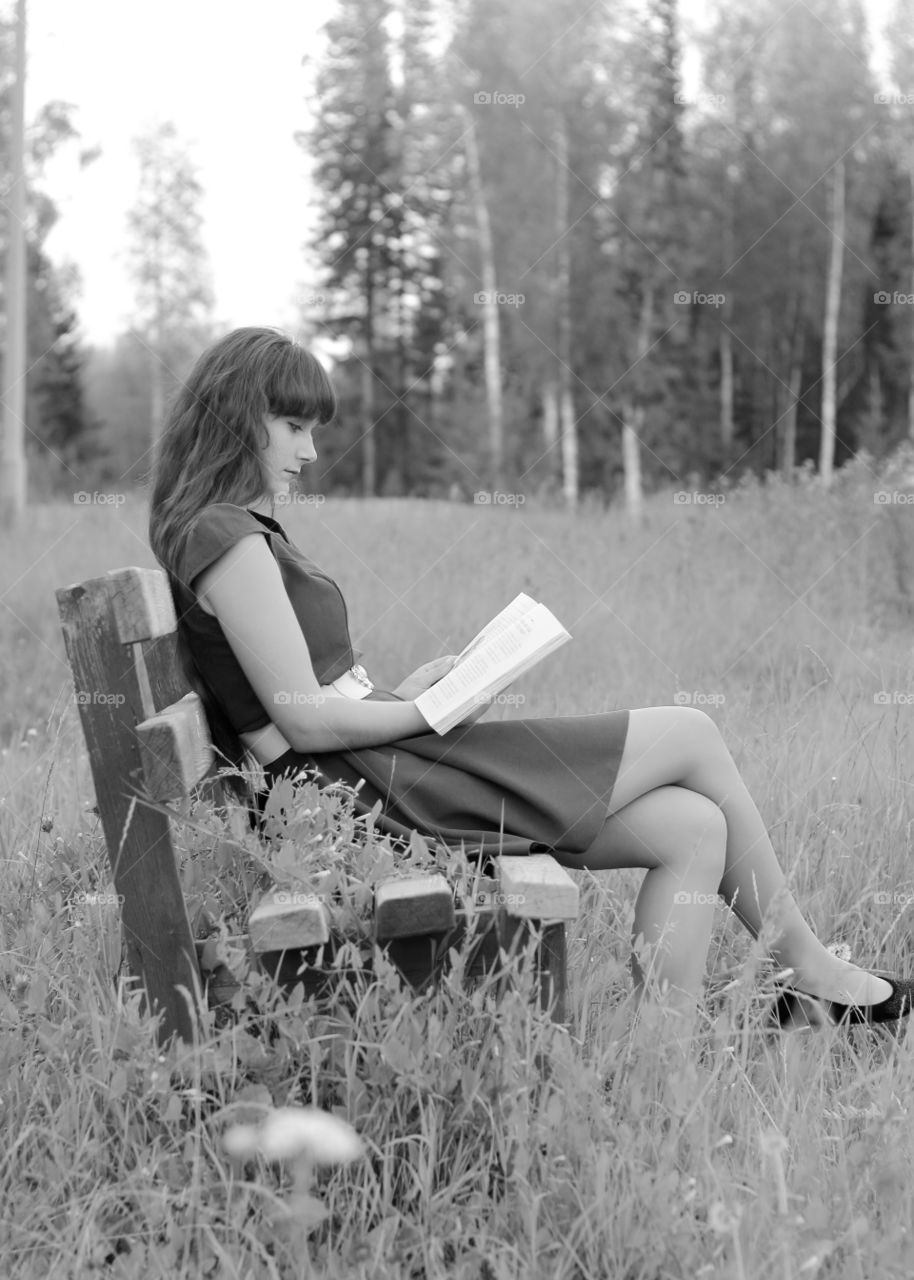 Young woman sitting on bench and reading book