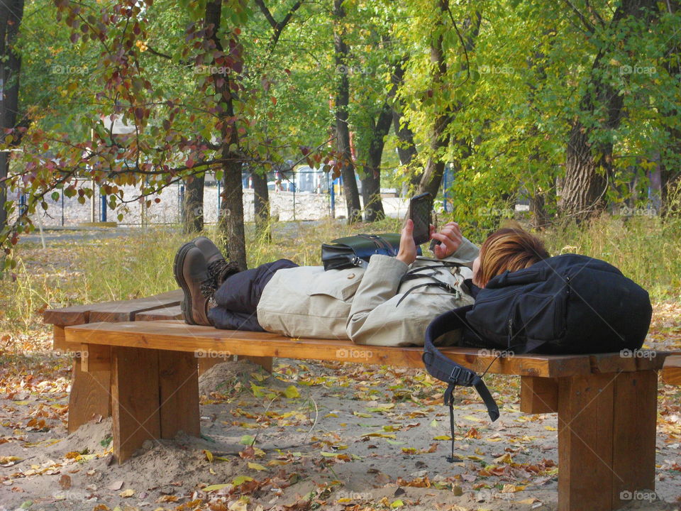 girl with a smartphone in the hands lying on a bench in the park