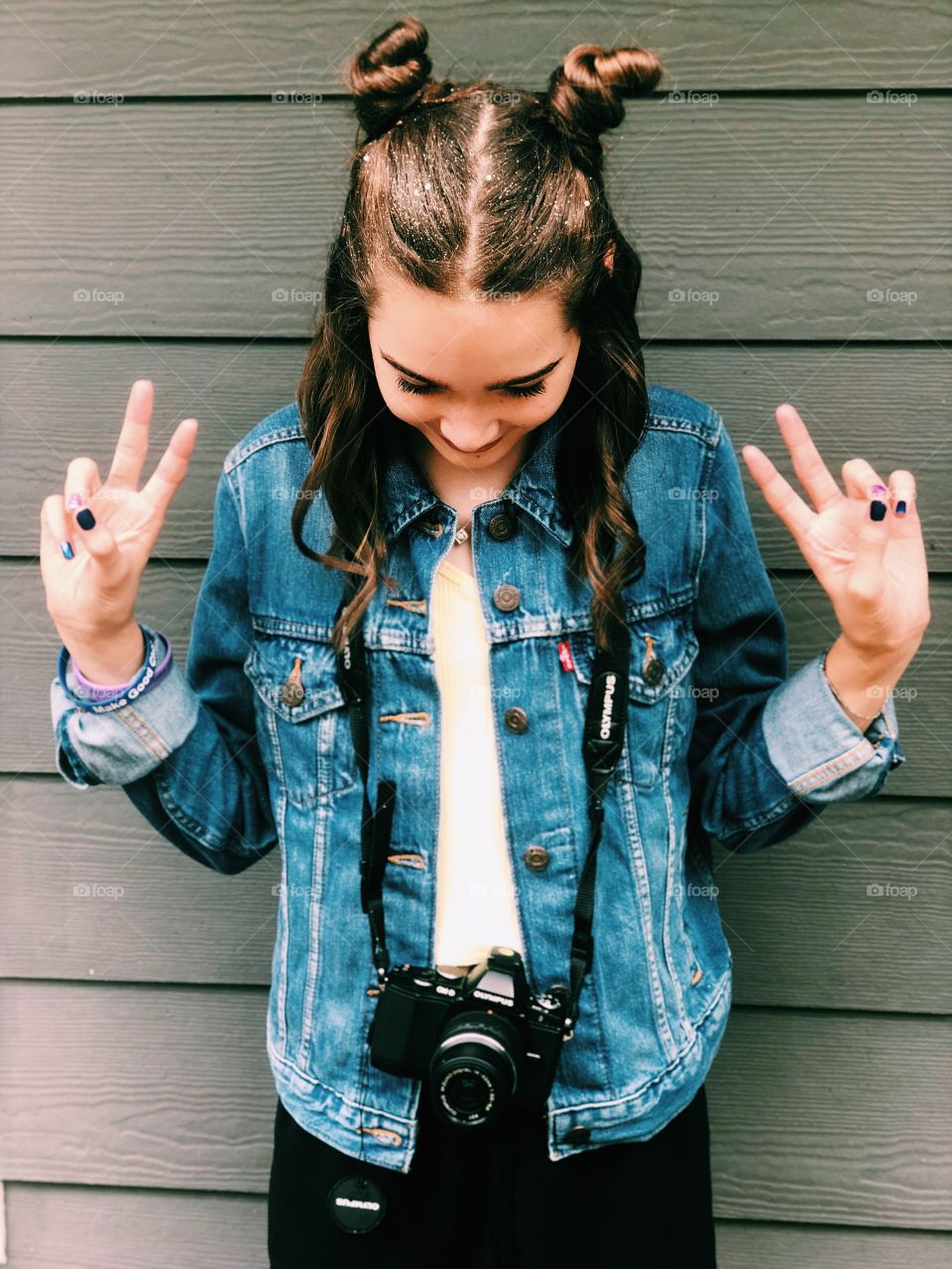Girl with space buns and glitter in hair wearing jean jacket with camera around neck. 