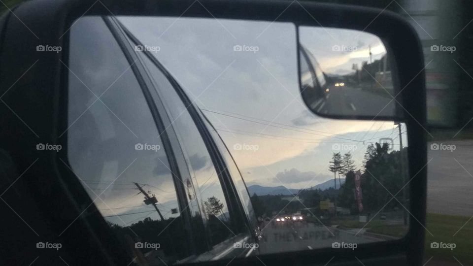 Picture of cars on the road with mountains in the distance in a car's side mirror during sunset.