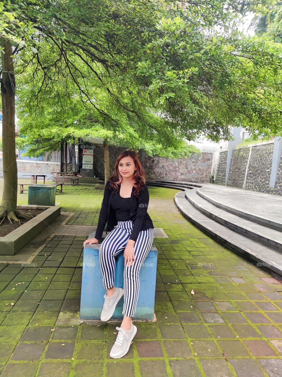 Full body portrait of a young woman sitting under a tree in a park