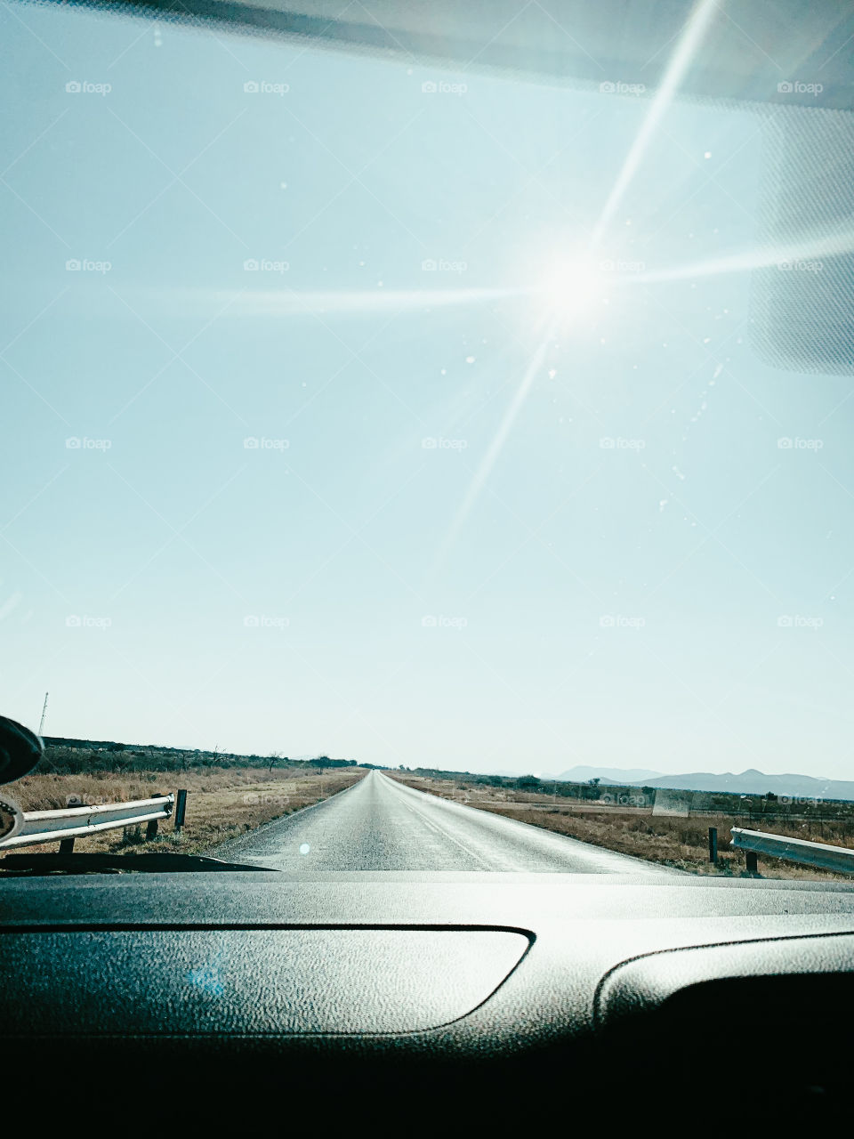 A clear view of the road from a car’s windscreen. With a bright sunshine and mountains in the background.