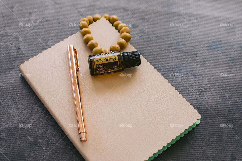Wild orange doterra essential oil bottle on notebook with rose gold pen and mustard bead bracelet 