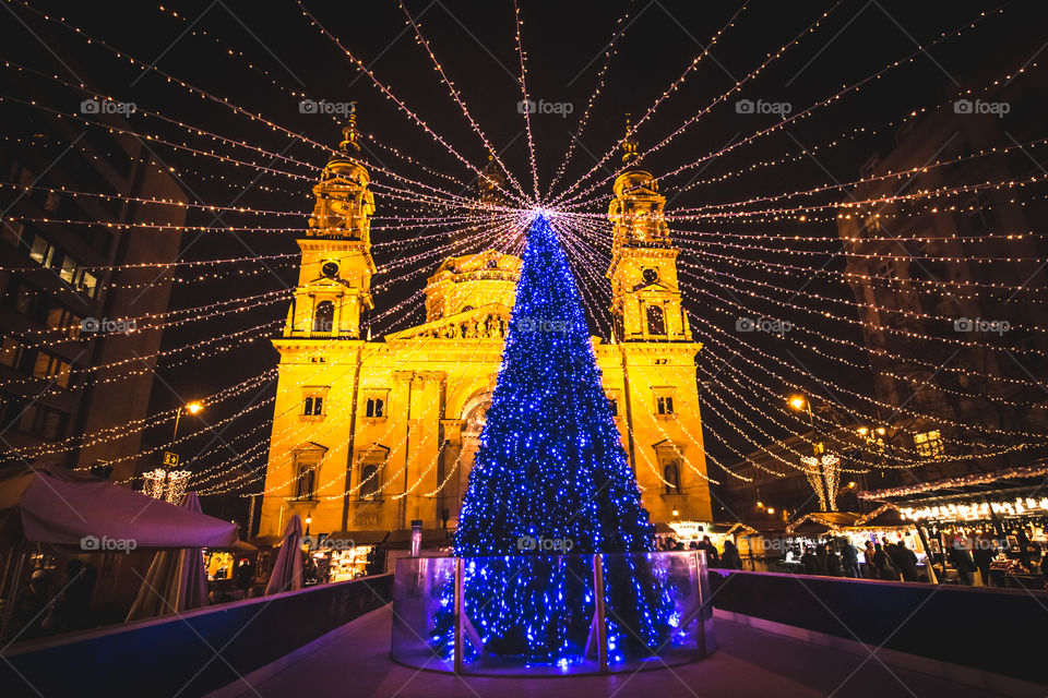 Outdoor Illuminated Blue Christmas Tree With Blue Lights At Square In Front Of A Church And People Enjoying Holidays
