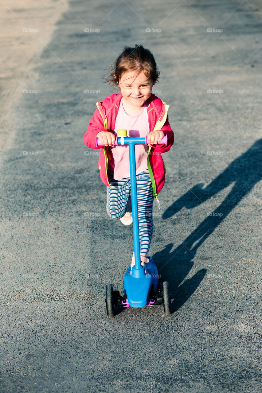 Little adorable girl having fun riding on scooter, playing outdoors. Real people, authentic situations