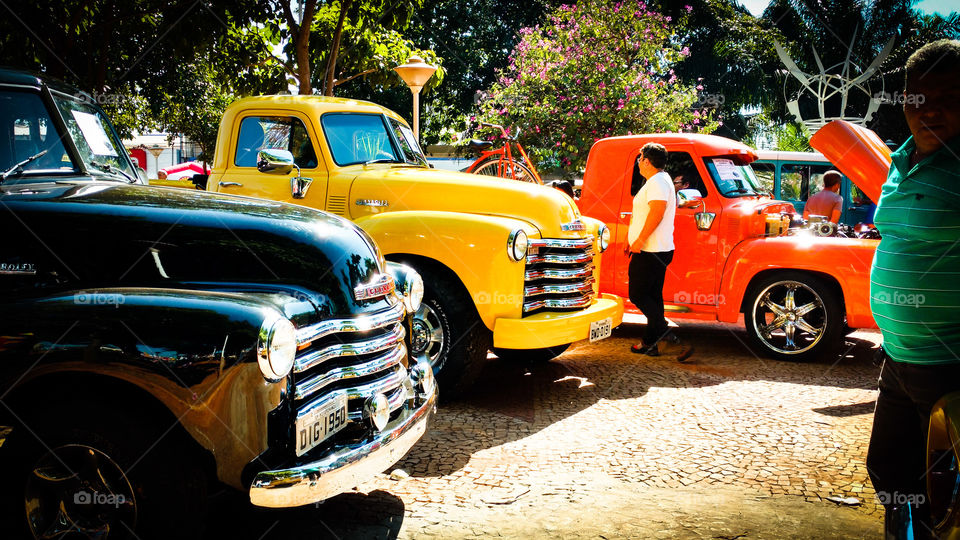 Camionetes de antigamente. Preta, amarela e laranja.